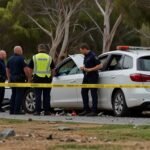 Mangled car wreckage surrounded by emergency vehicles at a crash site in Mandurah, West Australia, with debris scattered on the road.