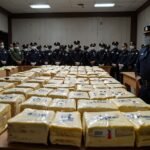 Ecuadorian National Police officers stand beside stacks of confiscated cocaine packages, neatly arranged for a press conference in Guayaquil.